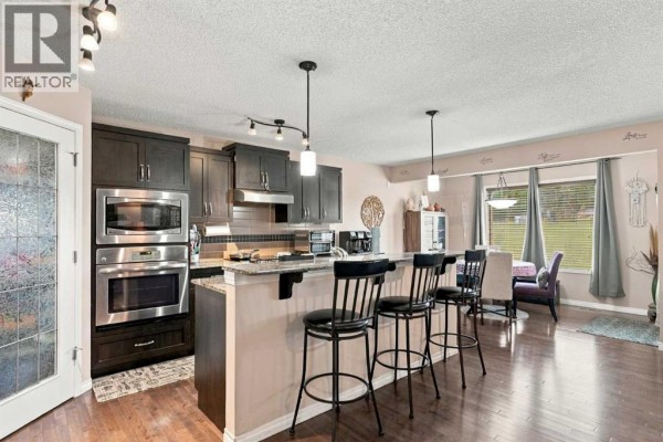 Kitchen with dark wood cabinets, stainless steel appliances, granite countertops, and a breakfast bar with stools. - 81 Walden Rise Se, Calgary