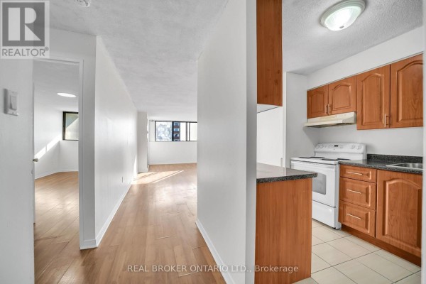 View of an apartment kitchen with wood cabinets and a hallway leading to a living area. - 810 - 10 Tapscott Road, Toronto