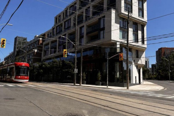 Street view of a beige apartment building with a red streetcar passing by on tram tracks. - 810 - 200 Sudbury Street, Toronto
