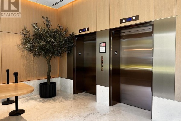Modern lobby with two stainless steel elevators, wood paneling, and a decorative tree. - 810 - 200 Sudbury Street, Toronto