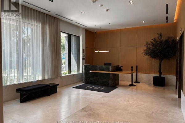 Apartment building lobby with a reception desk, wood paneling, a large plant, and beige flooring. - 810 - 200 Sudbury Street, Toronto