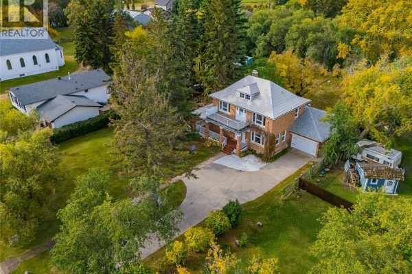 Aerial view of a brick house with a large lot and surrounding trees. - 810 4th Avenue, Rosthern
