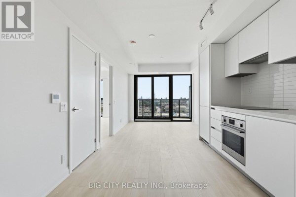View of the kitchen and living area with white cabinets and floor-to-ceiling windows. - 811 - 25 Frederick Todd Way, Toronto