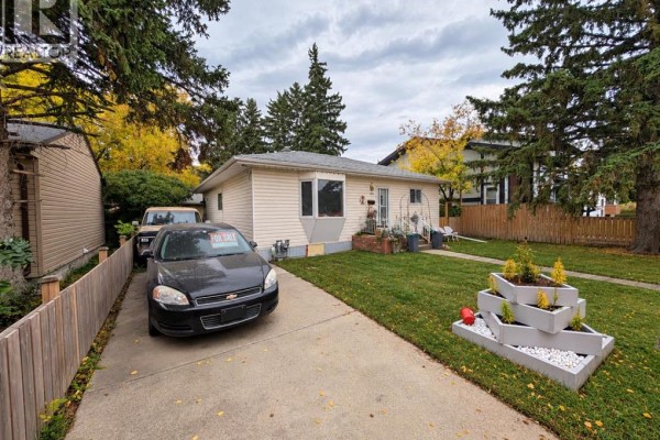 Side view of a house with a driveway, parked car, and lawn with planters. - 8119 34 Avenue Nw, Calgary