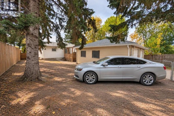 Backyard view showing a detached garage, a silver sedan, and a wooden fence. - 8119 34 Avenue Nw, Calgary
