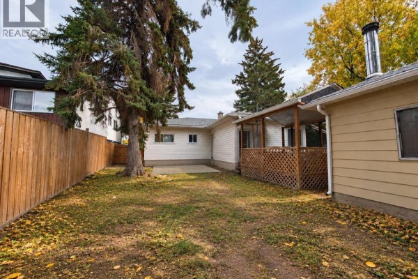 Rear view of the property with a covered deck, paved patio, and grassy yard. - 8119 34 Avenue Nw, Calgary