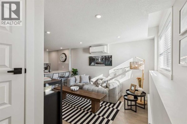 Living room with a grey sectional sofa, striped rug, wooden coffee table, and windows. - 812, 135 Mahognay Parade Se, Calgary