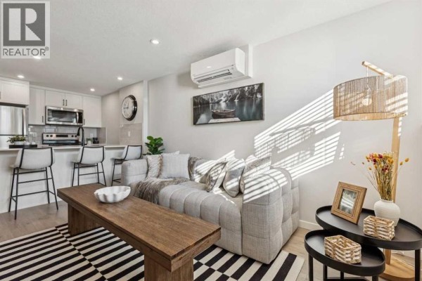 Living room with grey sofa, patterned rug, coffee table, bar seating, and kitchen cabinets. - 812, 135 Mahognay Parade Se, Calgary