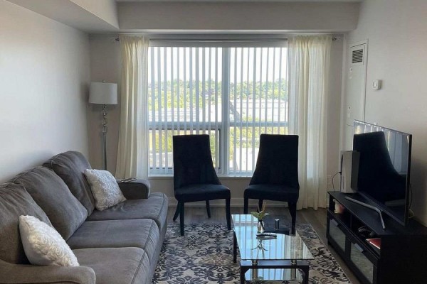 Living room with grey sofa, coffee table, two black chairs, and large window with blinds. - 812 - 181 Village Green Square, Toronto