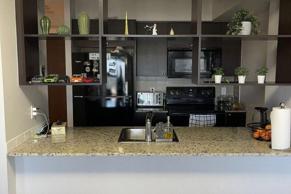Close-up of kitchen with stainless steel sink, black appliances, granite counters, and decorative open shelving. - 812 - 181 Village Green Square, Toronto