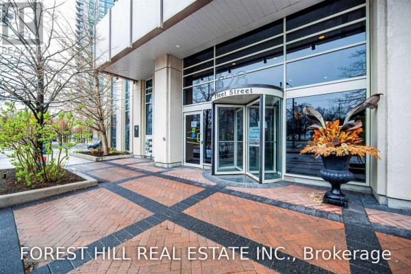 Entrance to a modern building with a revolving glass door, brick pathway, and trees. - 812 - 628 Fleet Street S, Toronto