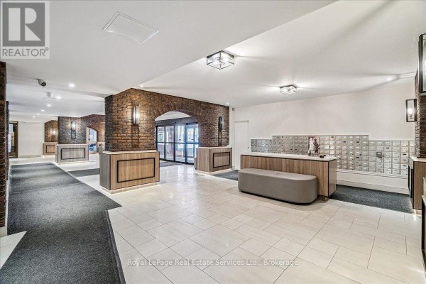 Building lobby with tiled floor, brick accent wall, mailboxes, and reception desk. - 812 - 966 Inverhouse Drive, Mississauga