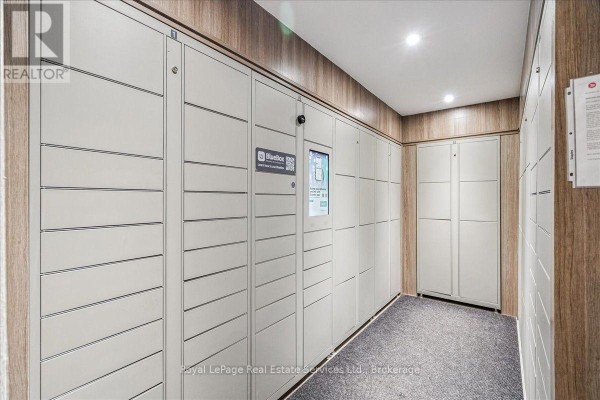 Hallway with carpet and wood-paneled walls featuring rows of secure package lockers. - 812 - 966 Inverhouse Drive, Mississauga