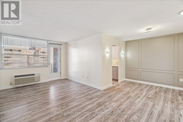Living room with light wood floors, large window, air conditioning unit, and decorative wall molding. - 812 - 966 Inverhouse Drive, Mississauga