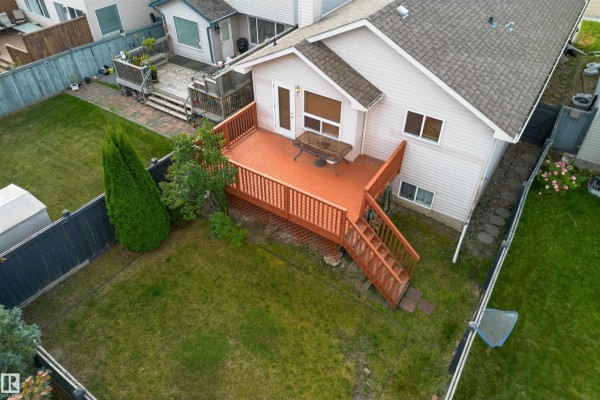 Backyard of a house with a wooden deck, green lawn, and a white shed. - 812 Barnes Link Sw, Edmonton