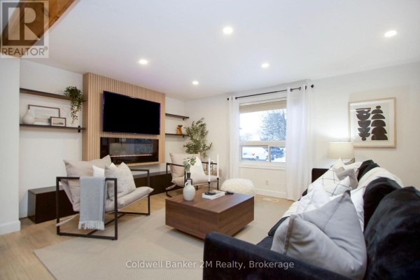 Cozy living room with a TV mounted on a wooden feature wall, large window, and modern furniture. - 812 Burnham Street, Cobourg