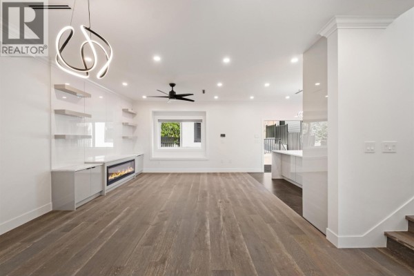 Living area with fireplace, built-in shelving, hardwood floors, and a view of the kitchen. - 812 Montroyal Boulevard, North Vancouver