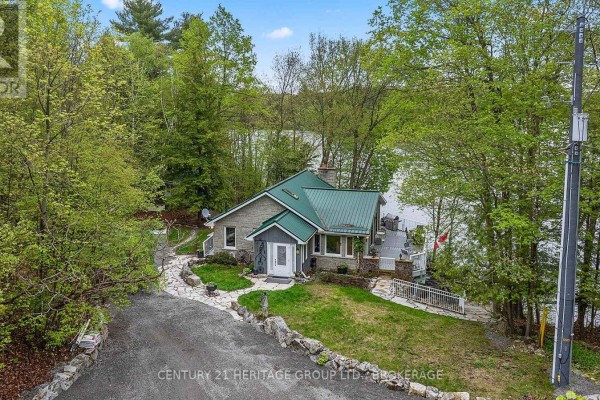 Wooden deck with dining set and chairs overlooking a lake with trees. - 8126 Perth Road, South Frontenac