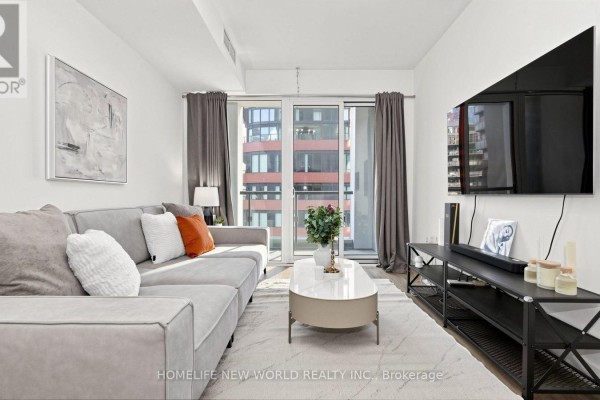 Living room with a grey sectional sofa, coffee table, and large television opposite a sliding glass door. - 813 - 158 Front Street E, Toronto