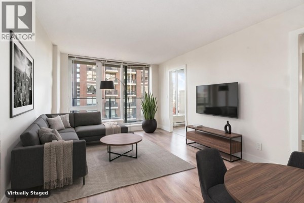 Living area with a dark grey sectional sofa, floor lamp, and view of city buildings. - 813 1088 Richards Street, Vancouver