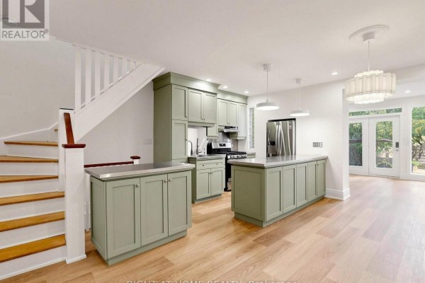 Staircase leading to an open-concept kitchen and living area with light wood floors. - 813 Carlaw Avenue, Toronto