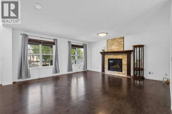 Living room with dark wood floors, stone fireplace, and large windows. - 813 Prestwick Circle Se, Calgary
