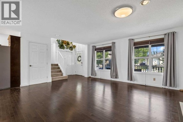 Living room with dark wood floors, view of entryway, and large windows. - 813 Prestwick Circle Se, Calgary