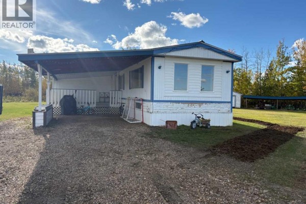Front view of a white mobile home with a dark blue carport, porch, and gravel driveway. - 8135 Township Road 782, Rural Saddle Hills County