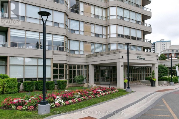Entrance to an apartment building with a covered walkway and flower beds. - 814 - 11 Townsgate Drive, Vaughan