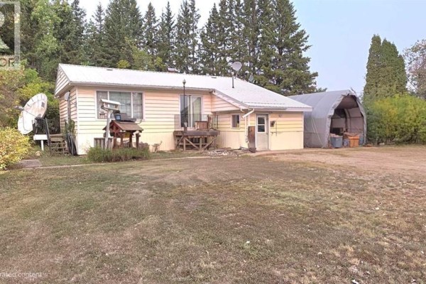 A yellow and white house with a covered carport and a wooden deck in a rural setting. - 81404 Rr223, Rural Northern Sunrise County