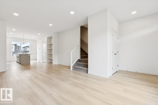 Open-concept living space with light wood floors, white walls, and a kitchen island. - 8148 228 St Nw, Edmonton