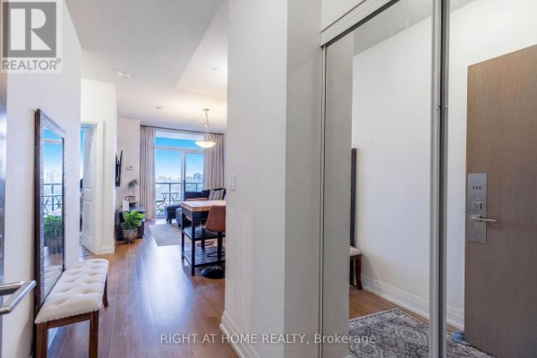 Apartment entryway with a mirrored closet, bench, and view of the living area. - 815 - 7167 Yonge Street, Markham