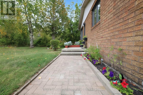 Paved walkway leading to the front entrance of a brick house with flower beds. - 815 Main Street, South Bruce Peninsula