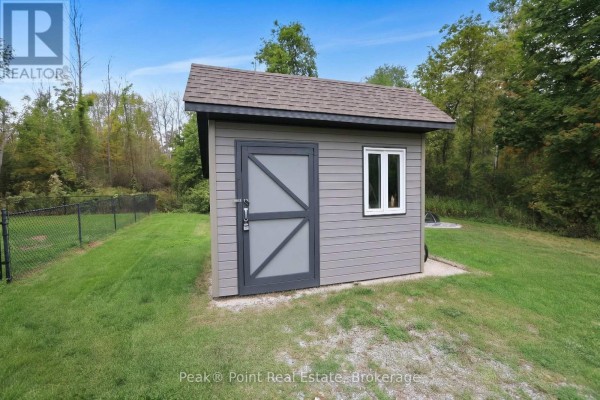 Close-up of a grey detached shed with a window and a dark grey door. - 815 Main Street, South Bruce Peninsula