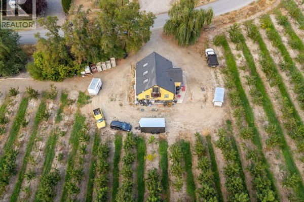 Aerial view of yellow house surrounded by fruit trees, vehicles, and trailers. - 815 Webster Road, Kelowna