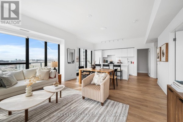 View of the open-concept living space, dining area with wooden table, and modern white kitchen. - 816 - 36 Brentcliffe Road, Toronto