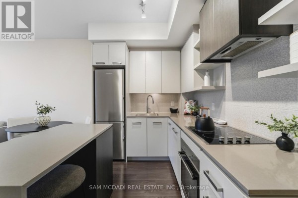 Modern kitchen with white cabinets, stainless steel appliances, and an island with stools. - 817 - 1830 Bloor Street W, Toronto
