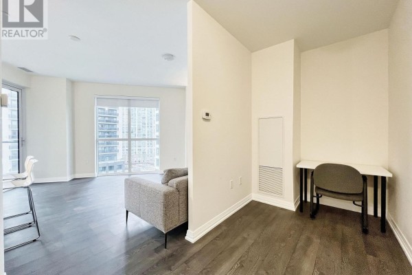Open concept living area with grey sofa, dark wood floors, and small desk. - 817 - 50 Thomas Riley Road, Toronto