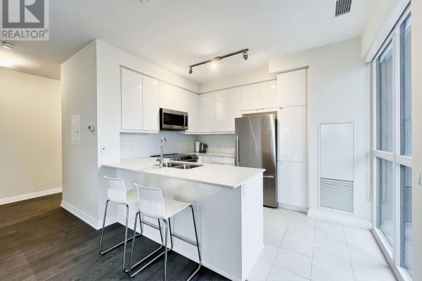 Modern kitchen with white cabinets, stainless steel appliances, and island with sink. - 817 - 50 Thomas Riley Road, Toronto