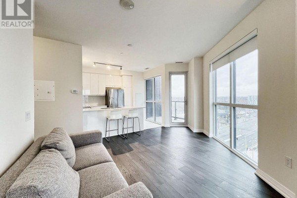 Living area with grey sofa and view of city skyline through large windows. - 817 - 50 Thomas Riley Road, Toronto