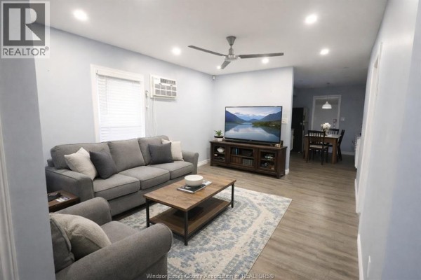 Living room with a grey sofa, coffee table, entertainment center with a TV, and a ceiling fan. - 817 Chatham Street East, Windsor