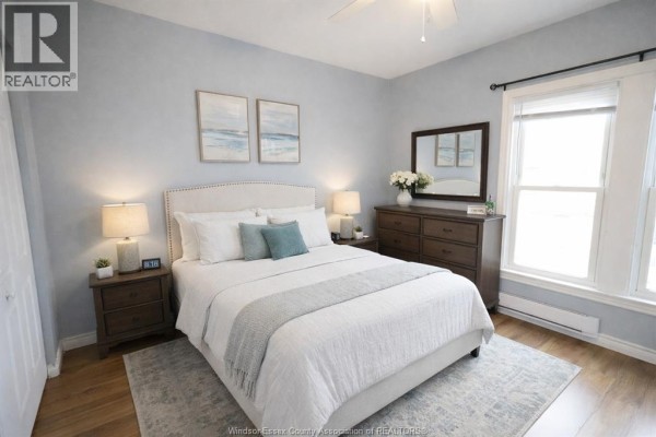 Primary bedroom with a queen-sized bed, bedside tables, a dresser with a mirror, and light blue walls. - 817 Chatham Street East, Windsor