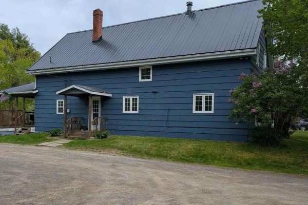 View of the back of the blue house with a covered porch and lawn. - 8178 Nova Scotia Trunk 8, South Brookfield