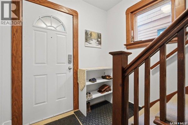 Interior front door area with a white door, wood trim, shoe rack, and stairs. - 818 B Avenue N, Saskatoon