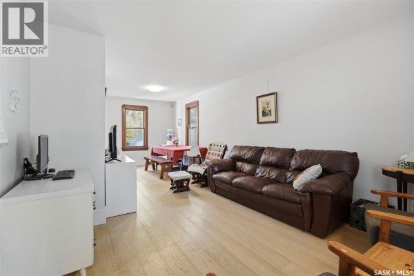 Living and dining room area with light wood floors, leather sofa, and dining table. - 818 B Avenue N, Saskatoon