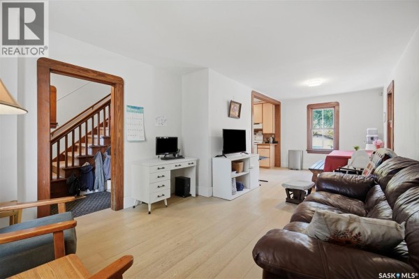 Living room view showing a desk, television, leather sofa, and doorway to the stairs. - 818 B Avenue N, Saskatoon