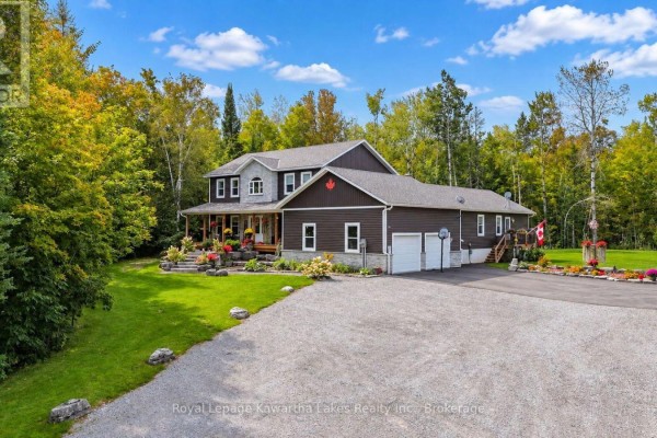 Side view of a dark-sided house with attached garage, covered porch, and driveway. - 819 County 49 Road, Kawartha Lakes