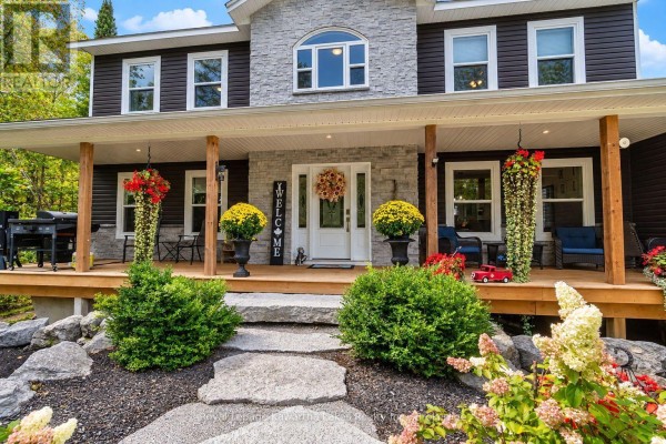Front porch of a dark-sided house with stone accents, columns, and flower arrangements. - 819 County 49 Road, Kawartha Lakes
