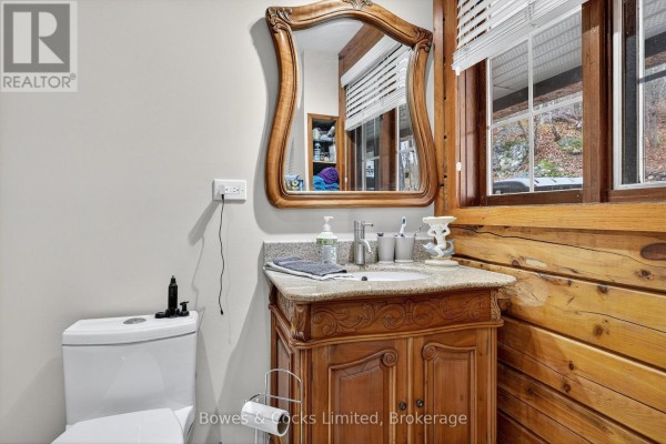 Ornate vanity with vessel sink and mirror in bathroom with log walls - 82 Bay Lake Road Bancroft