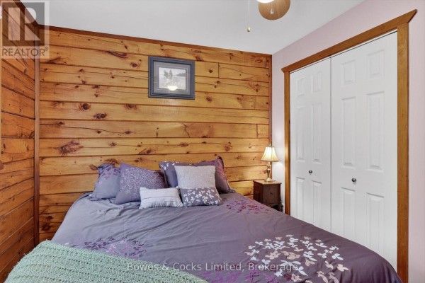 Bedroom with log wall, purple bedding, and double closet doors - 82 Bay Lake Road Bancroft